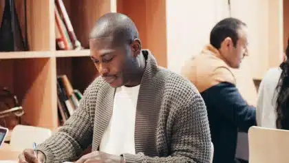 Personne assise à un bureau, concentrée sur ses notes, dans un environnement calme et bien éclairé