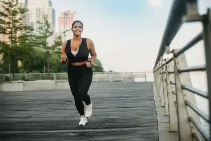 Personne en tenue de sport qui court dans un parc ensoleillé, vue de loin ou de profil.