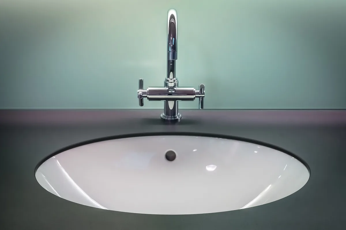 Brosse à dents et gratte-langue posés près d'un lavabo inondé de lumière du jour